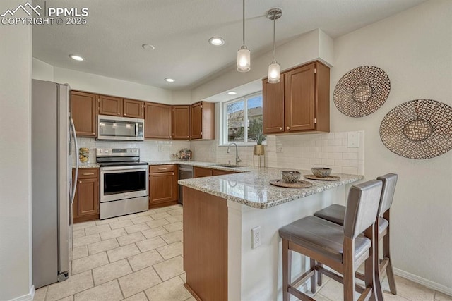 kitchen with brown cabinets, a sink, appliances with stainless steel finishes, a peninsula, and backsplash