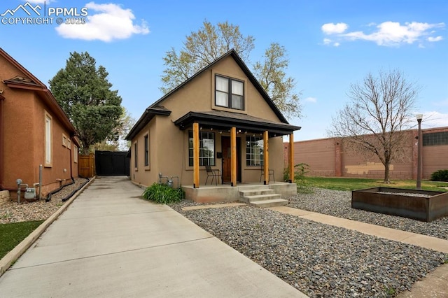 bungalow featuring fence, stucco siding, covered porch, and concrete driveway