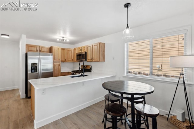 kitchen featuring a sink, light wood-style floors, stainless steel appliances, baseboards, and a peninsula