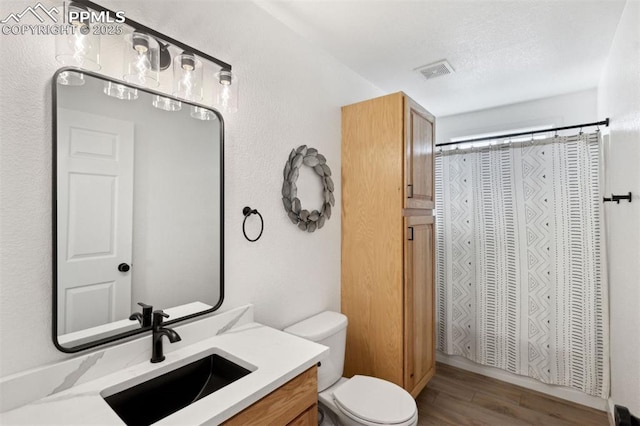 bathroom with vanity, toilet, wood finished floors, and visible vents