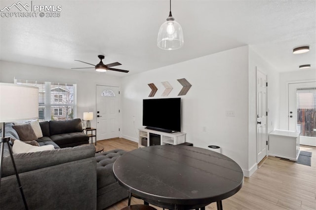 living area with a ceiling fan, baseboards, a healthy amount of sunlight, and light wood-type flooring