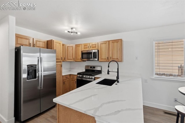 kitchen featuring appliances with stainless steel finishes, light stone counters, a sink, a peninsula, and baseboards
