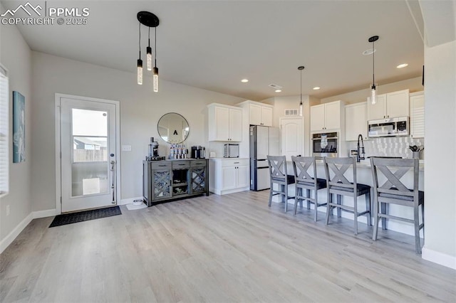 kitchen featuring a breakfast bar area, stainless steel appliances, baseboards, white cabinetry, and light wood-type flooring