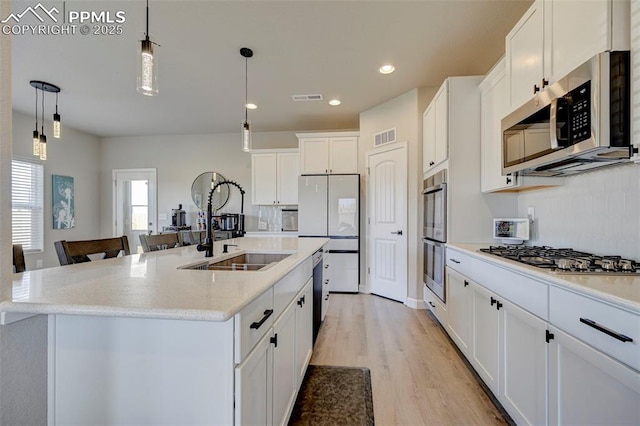 kitchen with stainless steel appliances, visible vents, a sink, and light wood finished floors