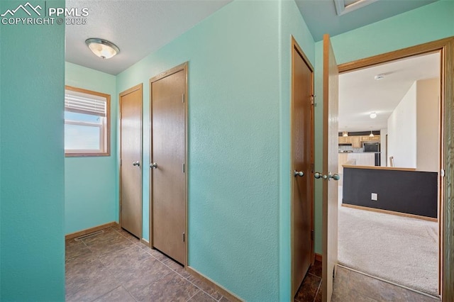 hallway featuring a textured wall and baseboards
