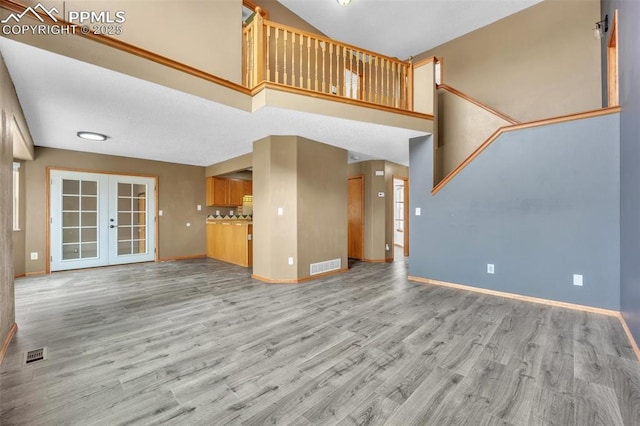 unfurnished living room featuring baseboards, light wood-style flooring, french doors, and a towering ceiling