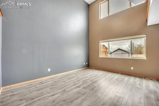 spare room with wood finished floors, baseboards, and a towering ceiling
