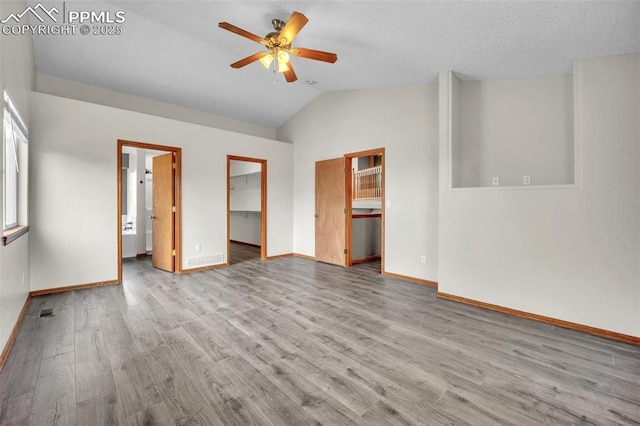 unfurnished bedroom with a spacious closet, lofted ceiling, wood finished floors, baseboards, and ceiling fan