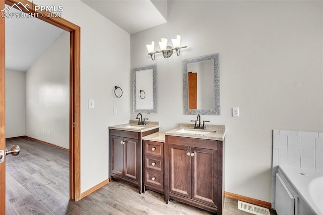 bathroom featuring wood finished floors, two vanities, baseboards, and a bath