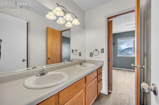 full bath featuring double vanity, wood finished floors, a textured ceiling, and baseboards