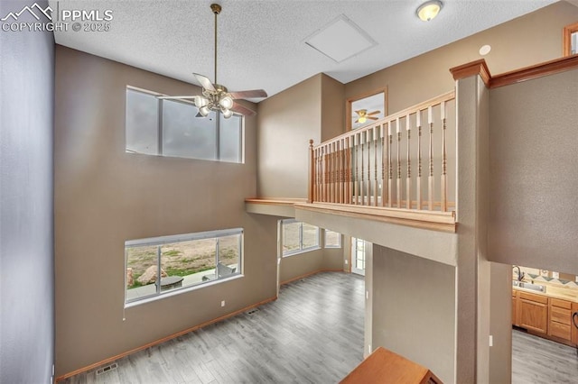 unfurnished living room featuring a ceiling fan, wood finished floors, a textured ceiling, baseboards, and a sink
