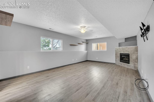 unfurnished living room featuring a textured ceiling, wood finished floors, a fireplace, ceiling fan, and baseboards