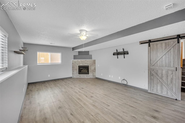 unfurnished living room with a textured ceiling, a ceiling fan, a barn door, wood finished floors, and baseboards