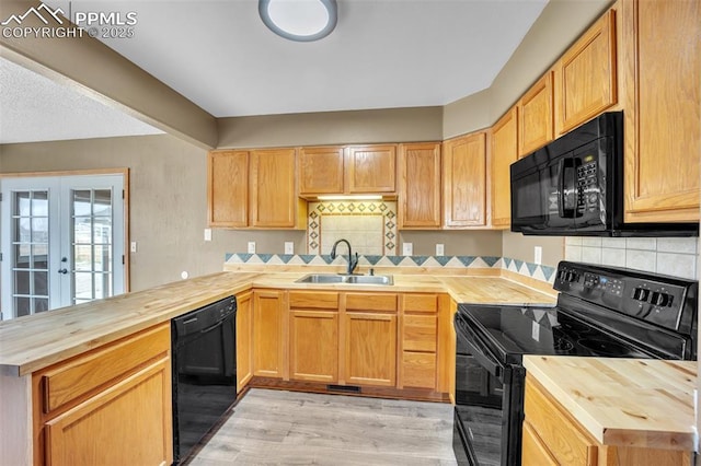 kitchen with butcher block counters, black appliances, a sink, a peninsula, and light wood finished floors
