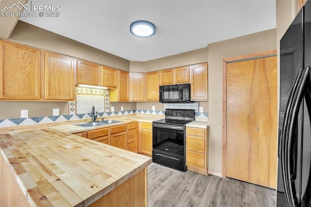 kitchen featuring black appliances, a sink, wood counters, light brown cabinetry, and a peninsula