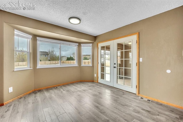 unfurnished room with french doors, plenty of natural light, baseboards, and a textured ceiling