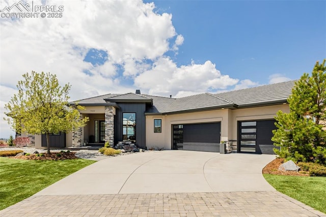 prairie-style home featuring a tile roof, driveway, stone siding, a front lawn, and an attached garage