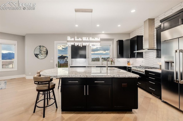 kitchen featuring appliances with stainless steel finishes, wall chimney range hood, dark cabinetry, and backsplash