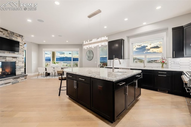 kitchen featuring light stone countertops, a kitchen island with sink, backsplash, and a sink