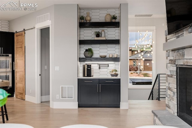 bar featuring a barn door, light wood-type flooring, visible vents, a stone fireplace, and double oven