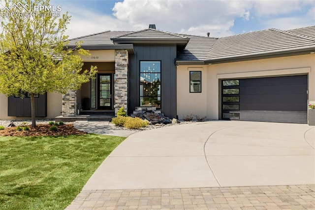 view of front facade with a tiled roof, stone siding, a front yard, concrete driveway, and an attached garage