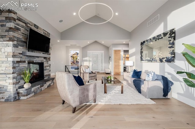 living room featuring wood finished floors, visible vents, high vaulted ceiling, and a stone fireplace