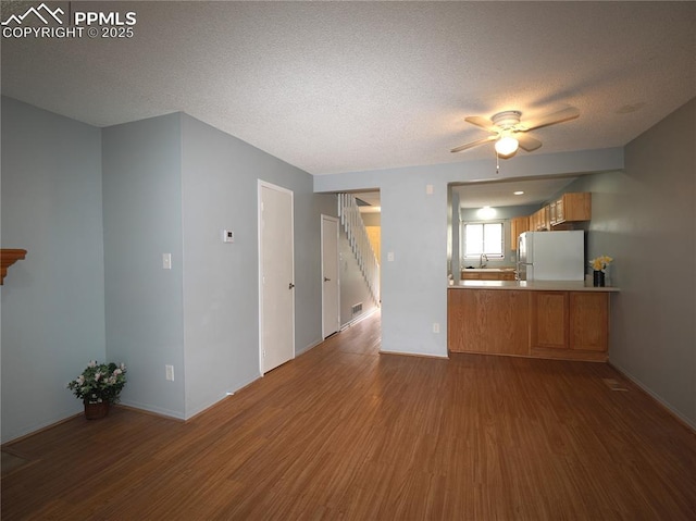 unfurnished living room featuring a textured ceiling, wood finished floors, ceiling fan, and baseboards