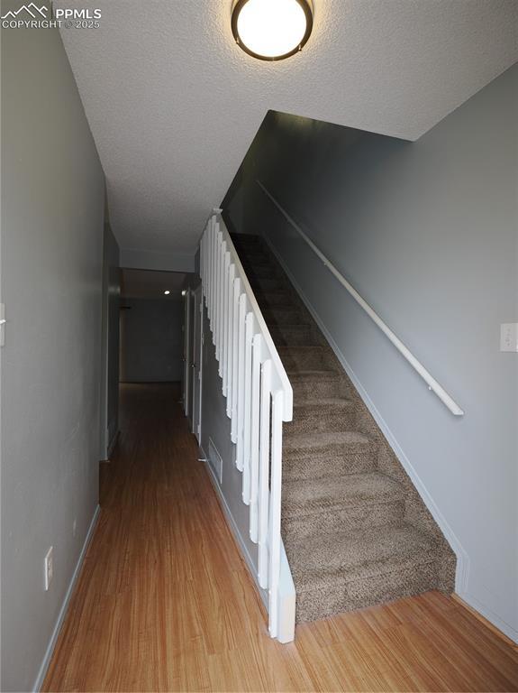 staircase with baseboards, visible vents, wood finished floors, and a textured ceiling