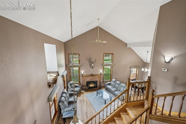 living room with a fireplace, high vaulted ceiling, ceiling fan with notable chandelier, stairs, and wood finished floors