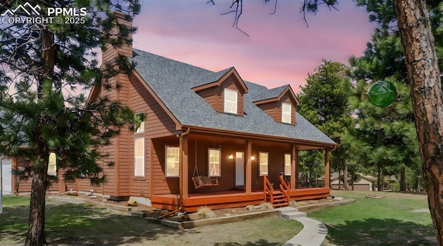 back of property with roof with shingles, a porch, an outbuilding, a chimney, and a yard