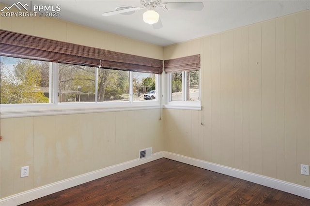 empty room with baseboards, ceiling fan, visible vents, and dark wood finished floors