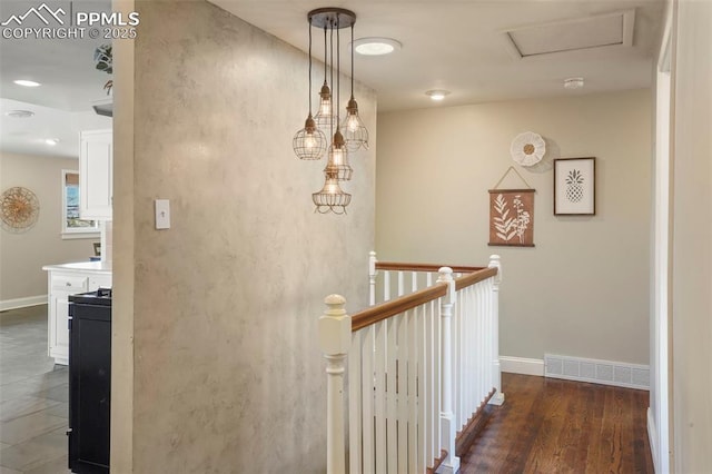 hallway with baseboards, visible vents, wood finished floors, and an upstairs landing
