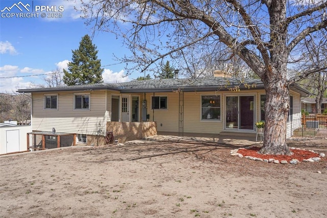 back of house featuring fence, a shed, a chimney, brick siding, and an outbuilding