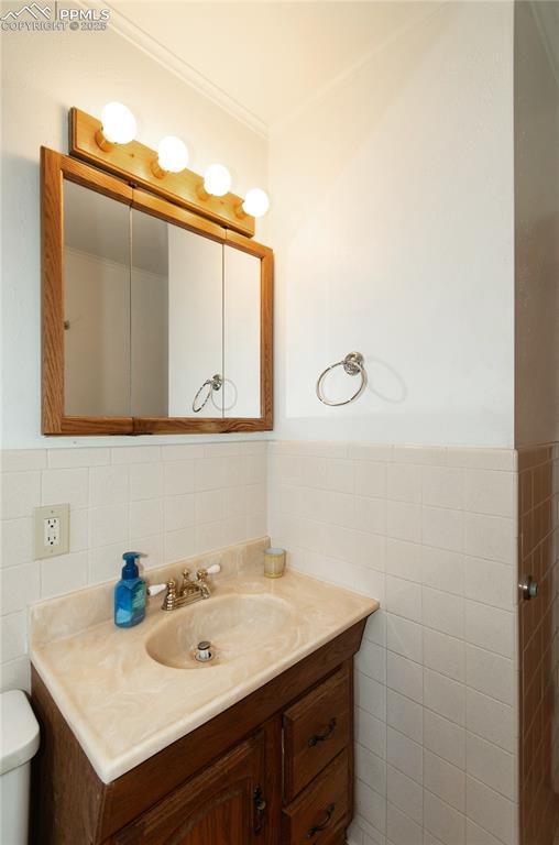 bathroom featuring tile walls, a wainscoted wall, vanity, and toilet