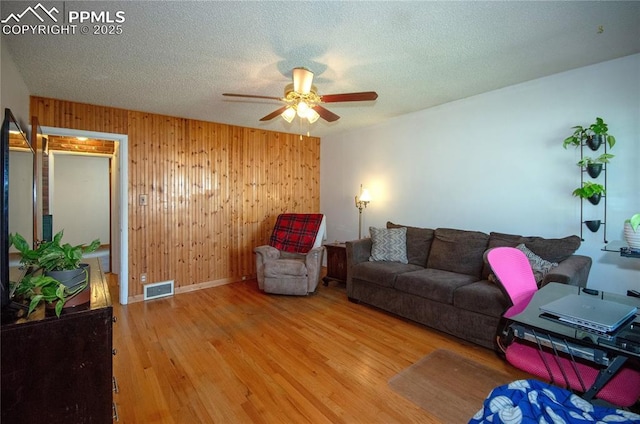 living room featuring visible vents, wood walls, wood finished floors, baseboards, and a ceiling fan