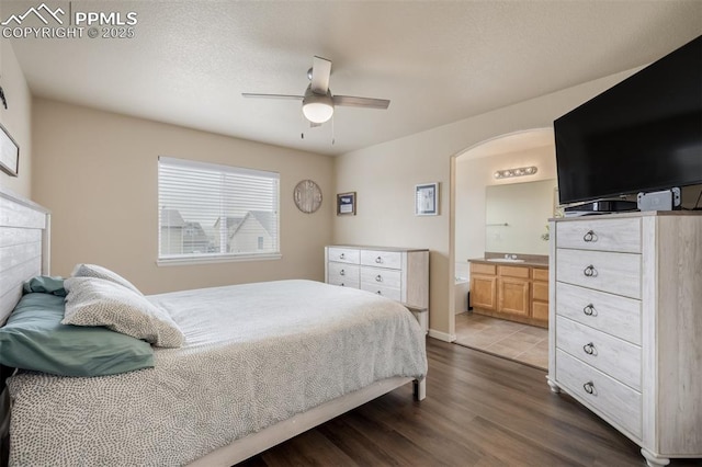 bedroom with arched walkways, ceiling fan, dark wood finished floors, and ensuite bathroom