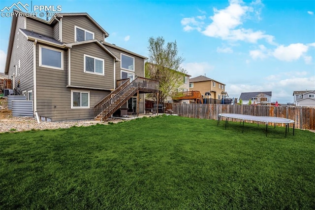 back of property with a trampoline, a deck, stairway, a fenced backyard, and a lawn