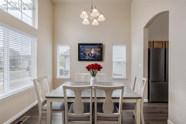 dining space featuring an inviting chandelier, dark wood-style flooring, baseboards, a high ceiling, and arched walkways