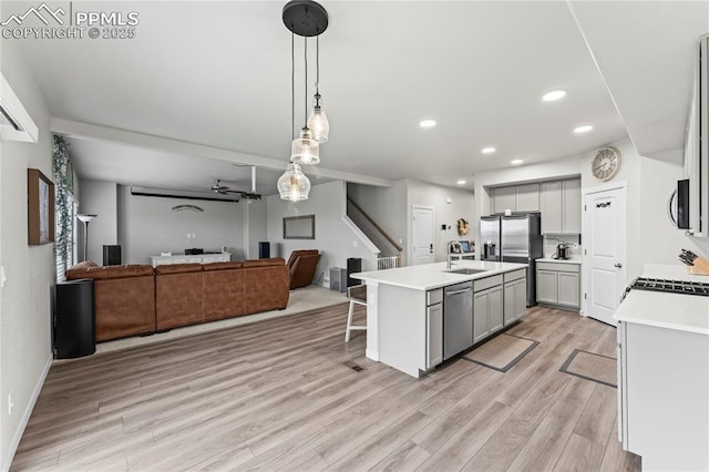 kitchen featuring open floor plan, light wood-type flooring, light countertops, gray cabinets, and appliances with stainless steel finishes
