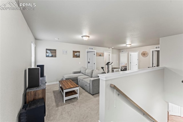 living area with visible vents, baseboards, and light carpet