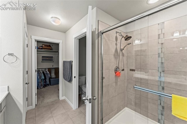 full bathroom with a shower stall, tile patterned floors, baseboards, toilet, and a spacious closet