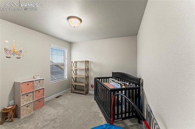 bedroom featuring visible vents, baseboards, a textured ceiling, a crib, and carpet flooring