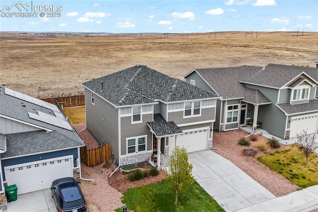 craftsman-style home with fence, stone siding, a rural view, an attached garage, and driveway