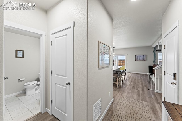 hall with baseboards, wood finished floors, and visible vents