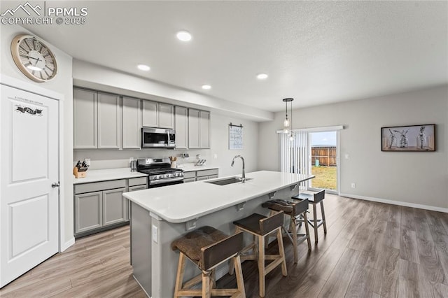 kitchen with gray cabinetry, appliances with stainless steel finishes, a sink, and light wood-style flooring