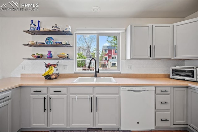 kitchen with decorative backsplash, white dishwasher, light countertops, a toaster, and a sink