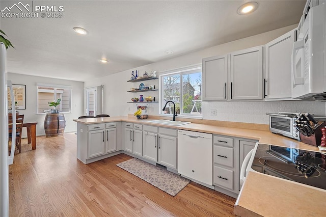 kitchen with a sink, light countertops, light wood finished floors, a peninsula, and white appliances