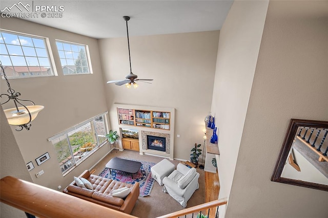 living area featuring a ceiling fan, a high ceiling, a glass covered fireplace, and baseboards
