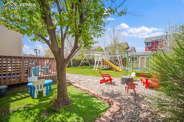 view of jungle gym featuring fence, a storage shed, a deck, a lawn, and an outdoor structure