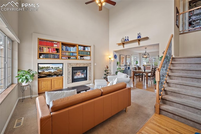 living room with visible vents, a towering ceiling, baseboards, stairway, and a ceiling fan